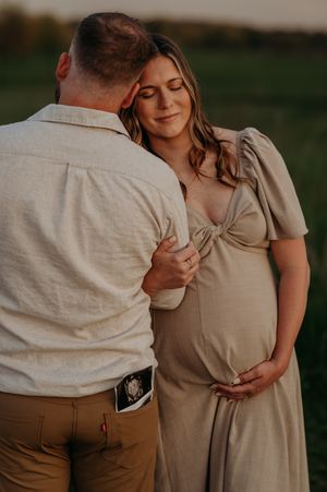 Romantic couple dressed in neutral tones share an intimate moment during an outdoor maternity photoshoot at sunset.