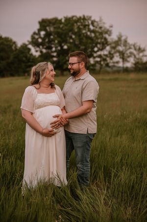Couple shares tender moments in a rustic field at sunset wearing white and casual attire.