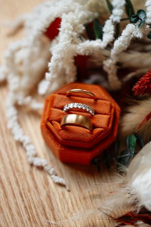 Wedding rings nestled in an orange velvet ring box surrounded by holiday decorations on a wooden surface.