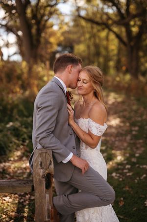 Romantic autumn wedding photos of couple sharing intimate moments on rustic wooden fence in wooded setting.