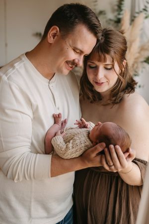 A tender newborn photography session with parents in white clothing against a light backdrop.