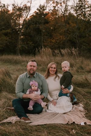 A family sits together on a blanket in a rustic outdoor setting during golden hour.