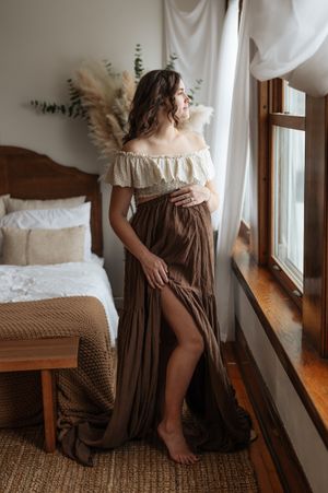 A person in a vintage-style brown dress poses artistically by a window in a series of moody boudoir photos.
