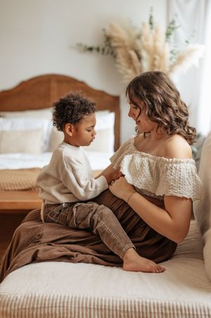 Mother and child share tender moments while relaxing together on a cozy bed with neutral tones and soft lighting.