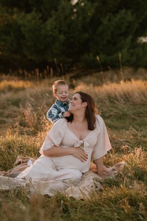 A tender outdoor maternity photo session in a golden field at sunset with warm lighting and natural scenery.