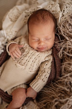 Sleeping newborn baby wrapped in cozy beige knit blankets in soft sepia tones.