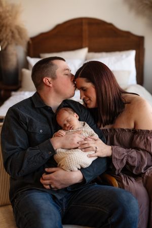 A tender family moment captured in warm lighting as parents share an intimate moment with their sleeping newborn baby.