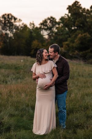 A romantic couple shares an intimate moment together in a grassy field at sunset.