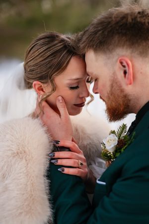 A tender intimate moment between newlyweds, with the bride wearing a white fur wrap and the groom in an emerald suit.