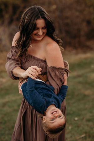 A mother in a brown dress holds and plays with a small child wearing navy blue in a tender outdoor moment.