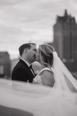 A romantic black and white wedding photo showing a couple kissing with a flowing veil and city skyline in the background.