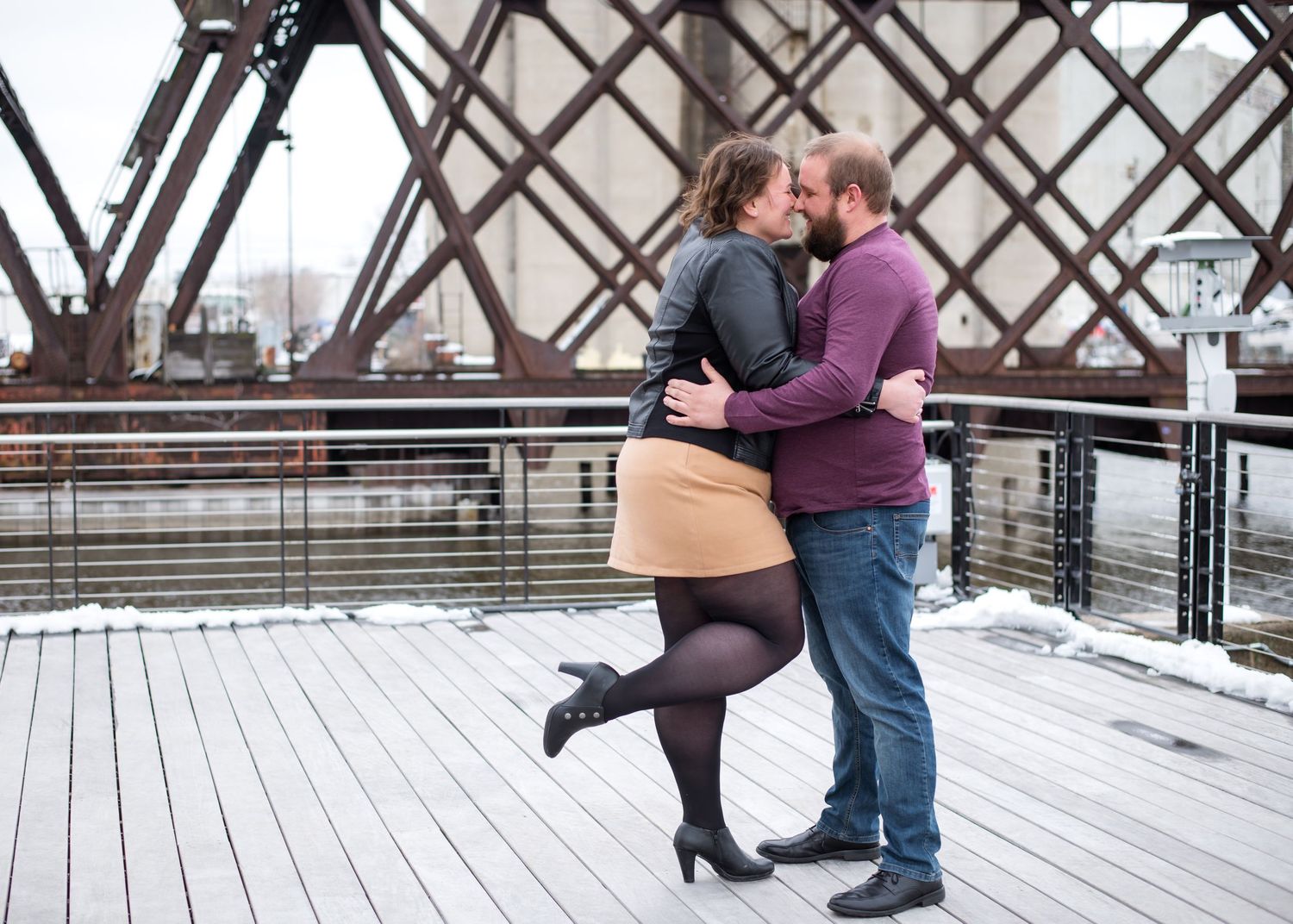 A couple shares an intimate moment on a snowy wooden boardwalk during winter.