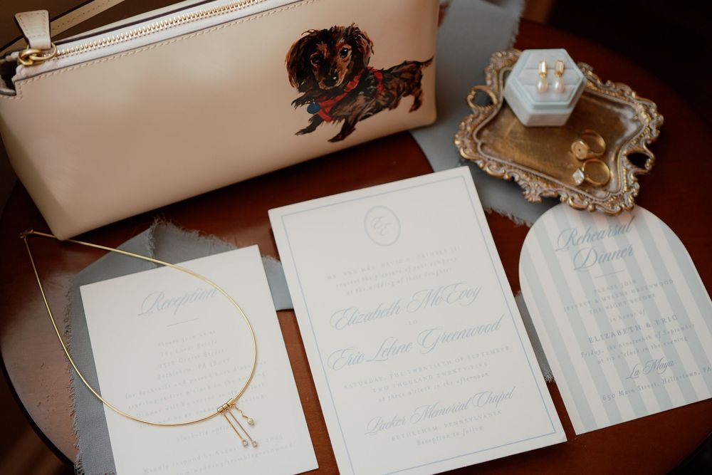 White wedding invitation suite with menus and stationery displayed on wooden surface near gold frame and leather pouch.