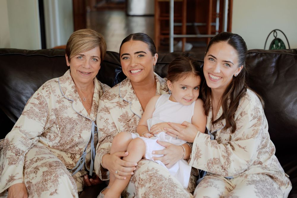 Four generations of family members wearing matching floral robes sit together on a brown leather couch.