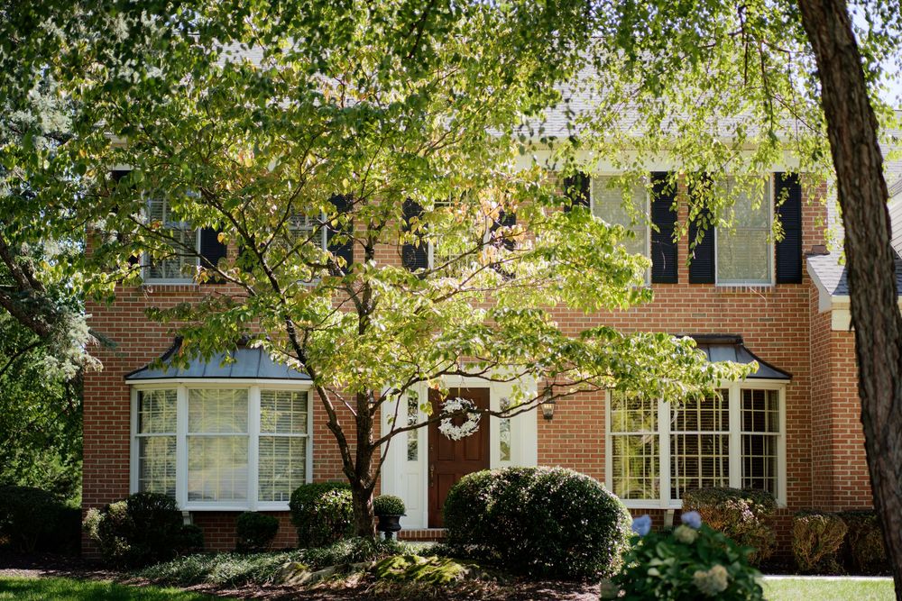 Exterior view of red brick row houses with front porches and mature trees on a sunny residential street.