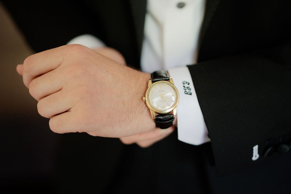 Close-up details of formal wedding attire showing hands with rings, luxury watch, and crisp suit cuffs in black and white.
