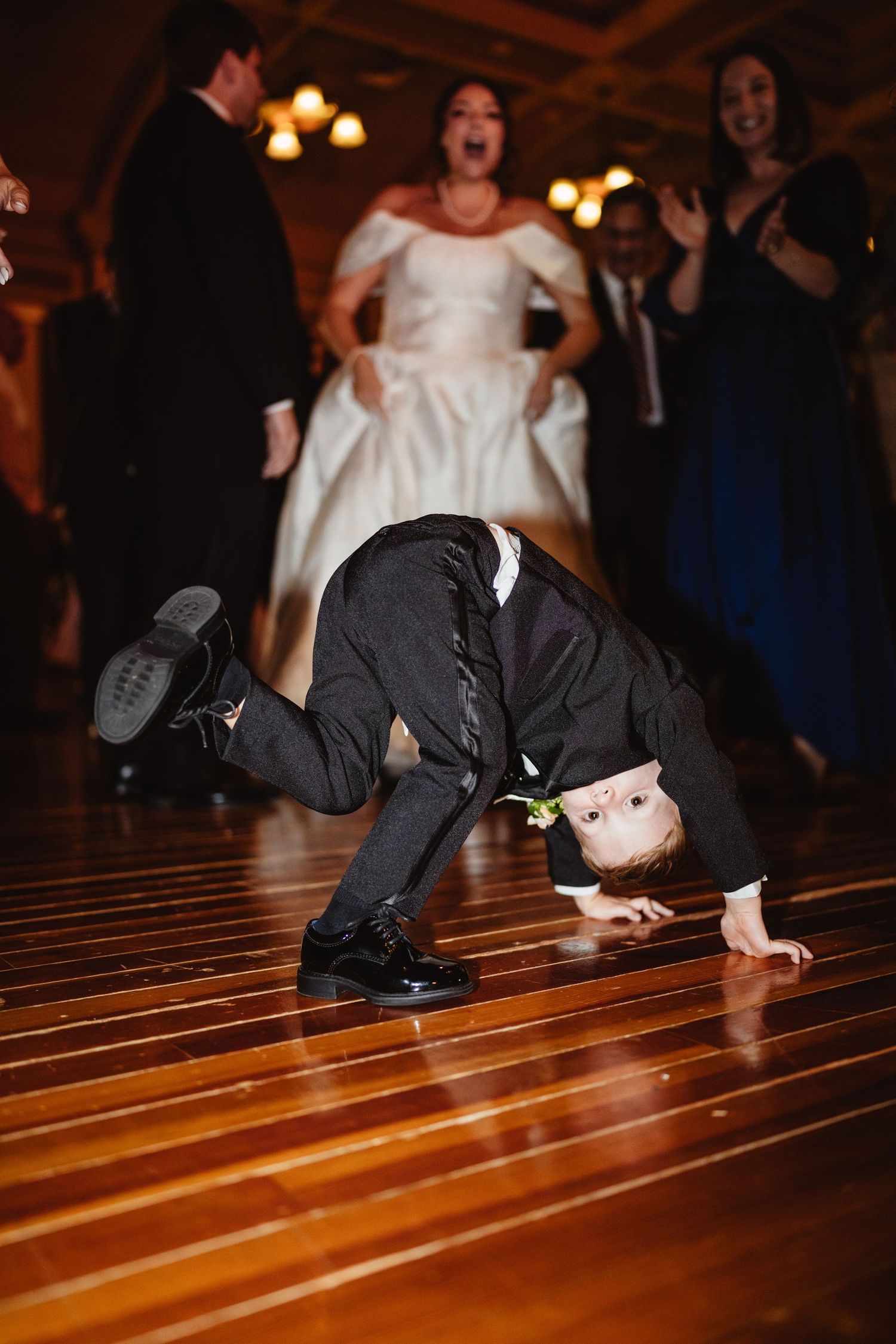 Wedding guest performs an impressive breakdancing move on the wooden dance floor at a reception.