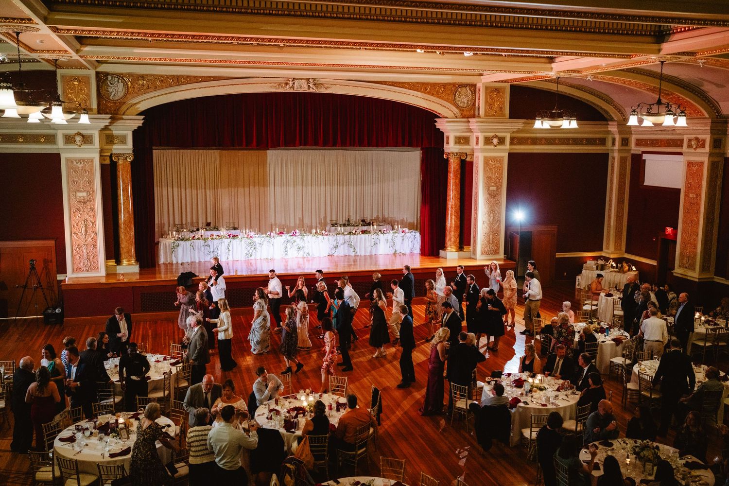 Panoramic view of an elegant ballroom reception with warm lighting and tables arranged for a formal event.