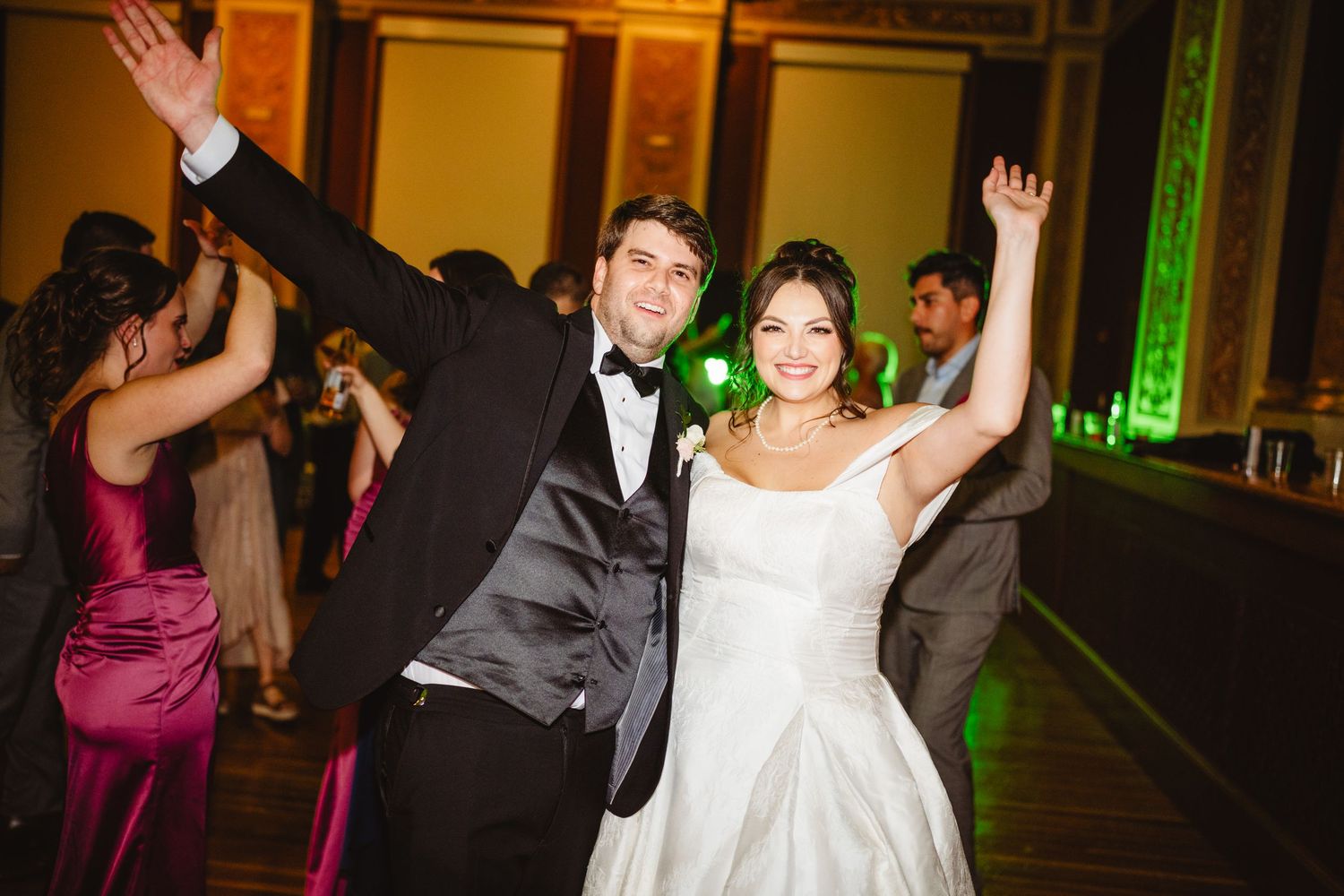 People dance and celebrate on a wedding reception dance floor with colorful lighting and formal attire.