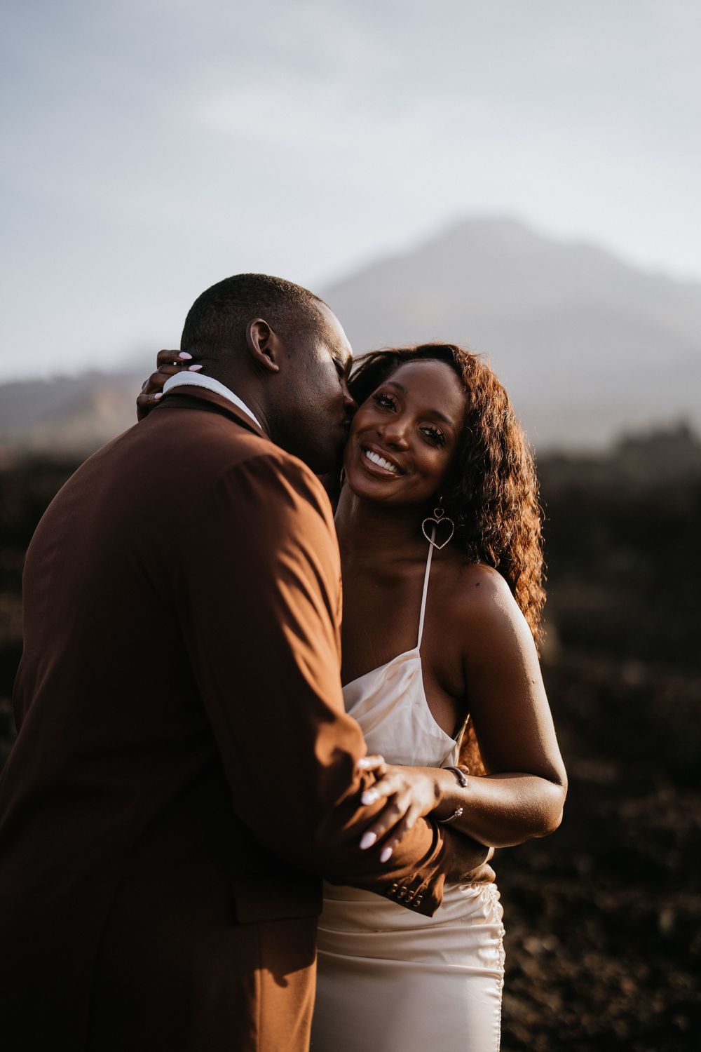 A romantic moment shared between a couple in formal attire with mountains in the background.