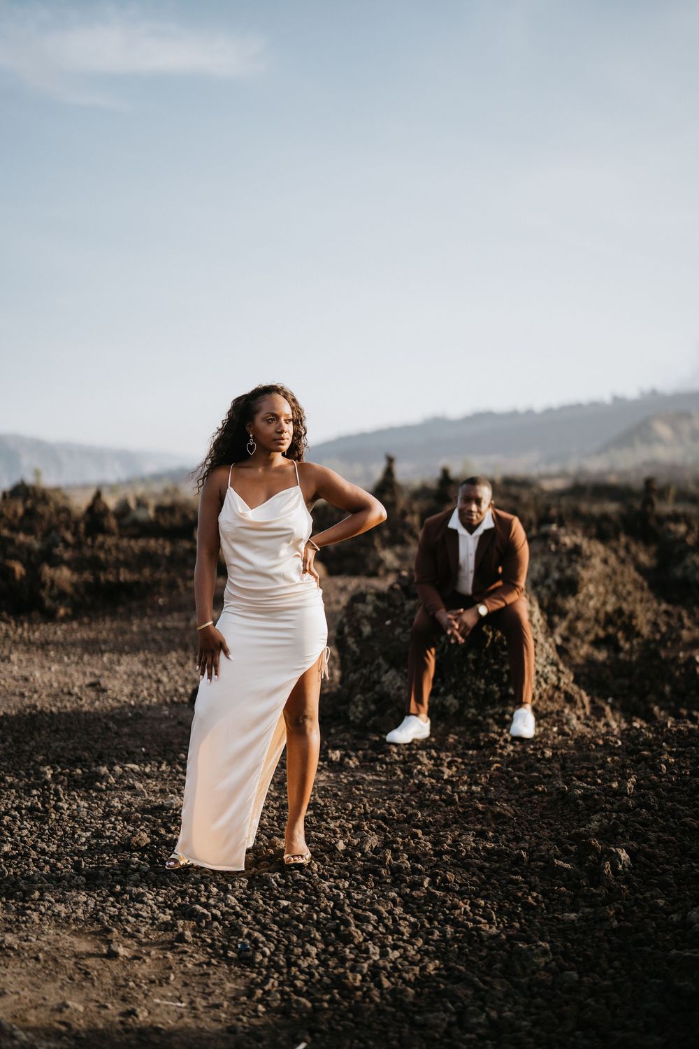 A romantic photoshoot on volcanic terrain with mountains in the background at sunset.