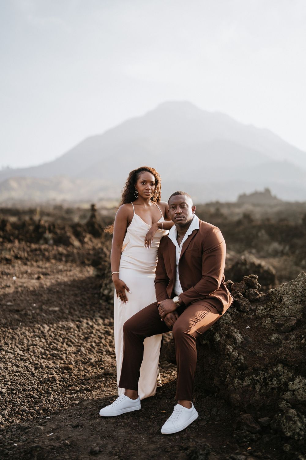 Casual outdoor portrait session on rugged volcanic terrain with mountain backdrop.