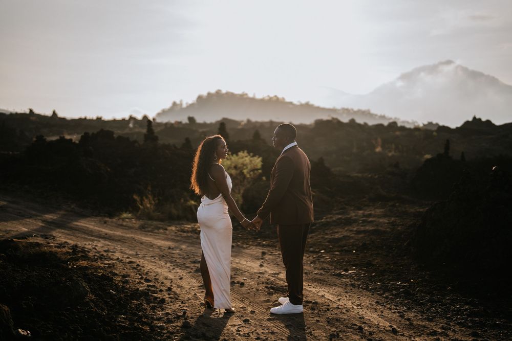 Two people walking hand in hand across rugged volcanic landscape at dusk.
