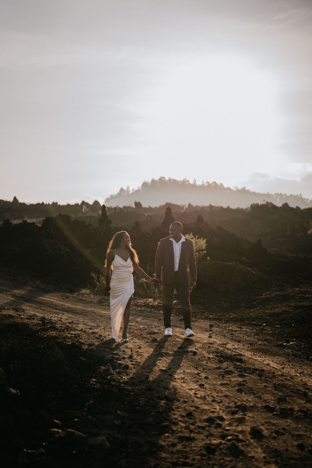 Silhouettes walking across rocky terrain with mountains and setting sun in background.
