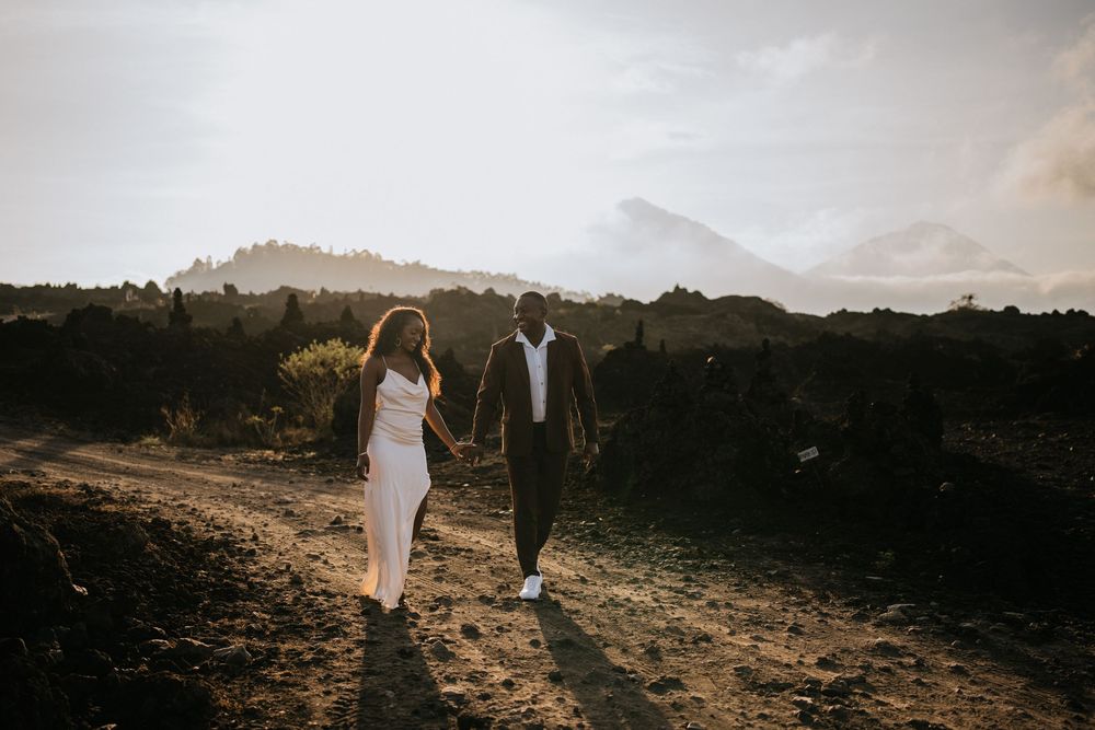 A couple explores volcanic terrain during golden hour with mountains in the distance.