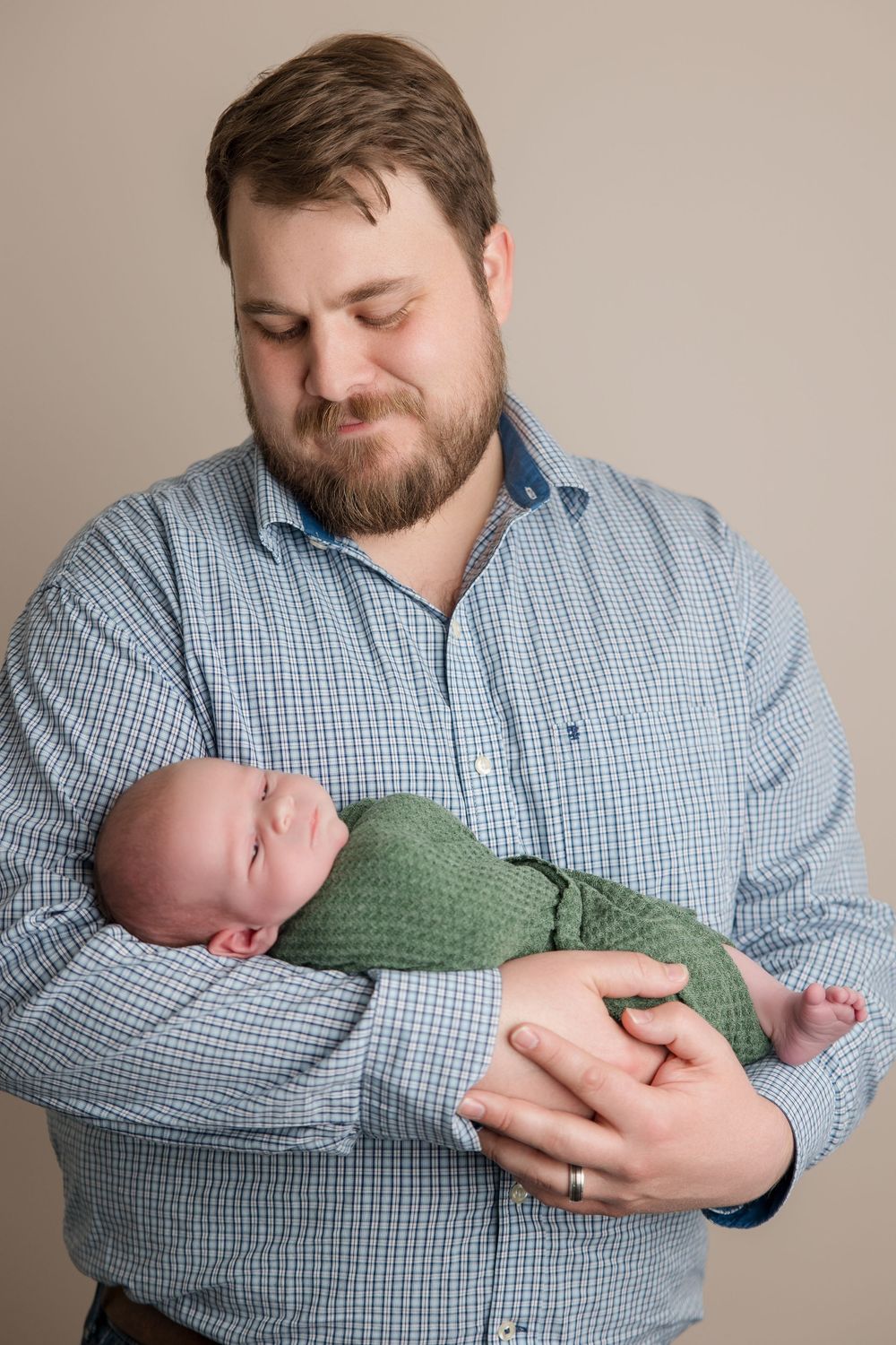 A touching series of photos showing a parent in a blue checkered shirt holding and gazing at a newborn in green attire.