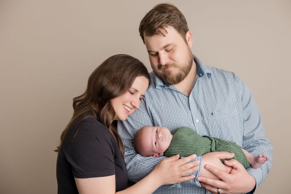 A loving family moment with baby in green outfit against neutral background.