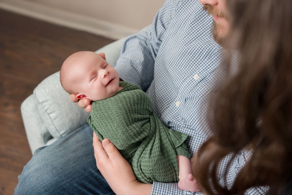 A parent lovingly holds and comforts a small baby wearing a green sweater while sitting on a wooden floor.