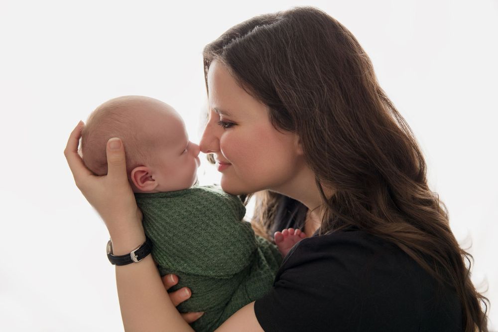 Parent holds newborn baby in green outfit while sharing tender moments against light background.
