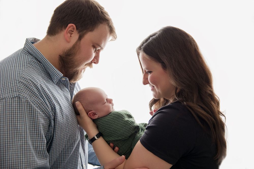Three photos showing tender moments between a romantic couple holding their baby in a white studio setting.