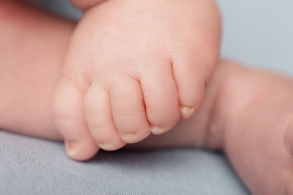 Delicate close-up of newborn baby's hand against soft gray textile background.