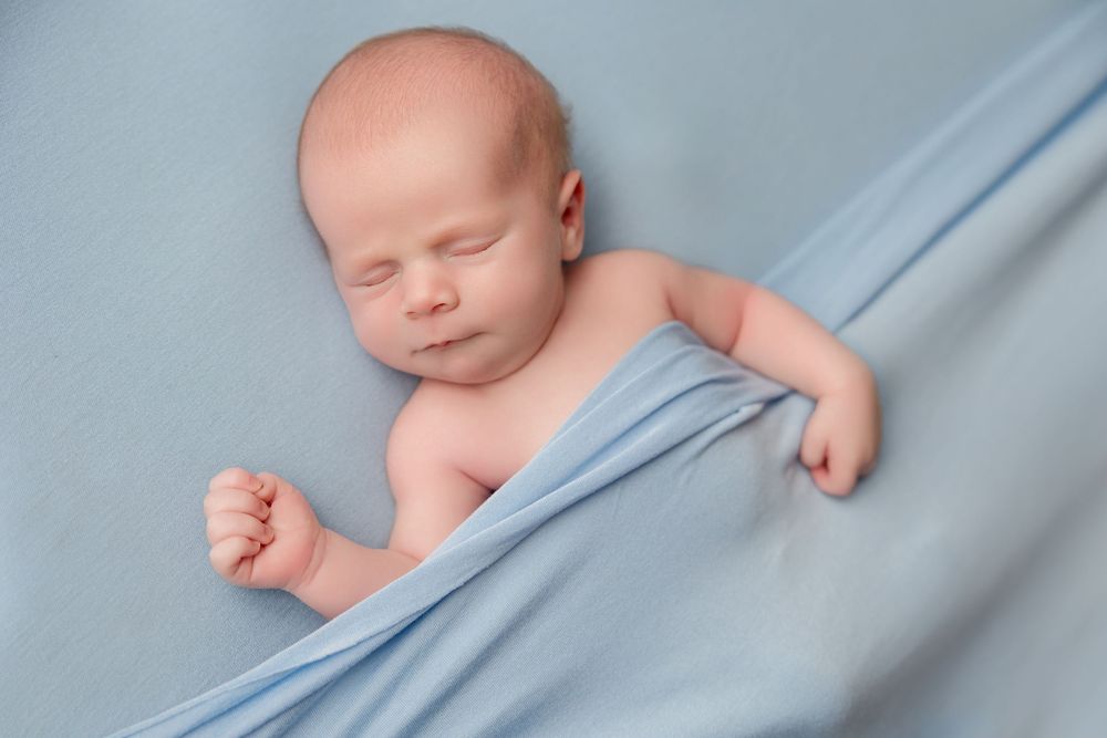 A sleeping newborn baby wrapped in soft blue fabric in various artistic poses.