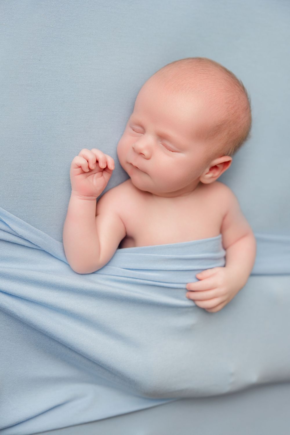 Sleeping newborn baby wrapped in soft light blue fabric in series of peaceful sleeping poses.