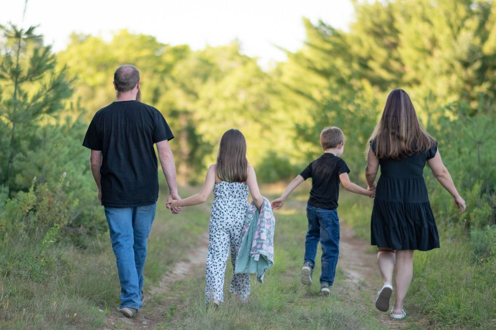 Family of four holding hands walking down a scenic green nature trail together. Photo by Xenophon Photography in Maine.