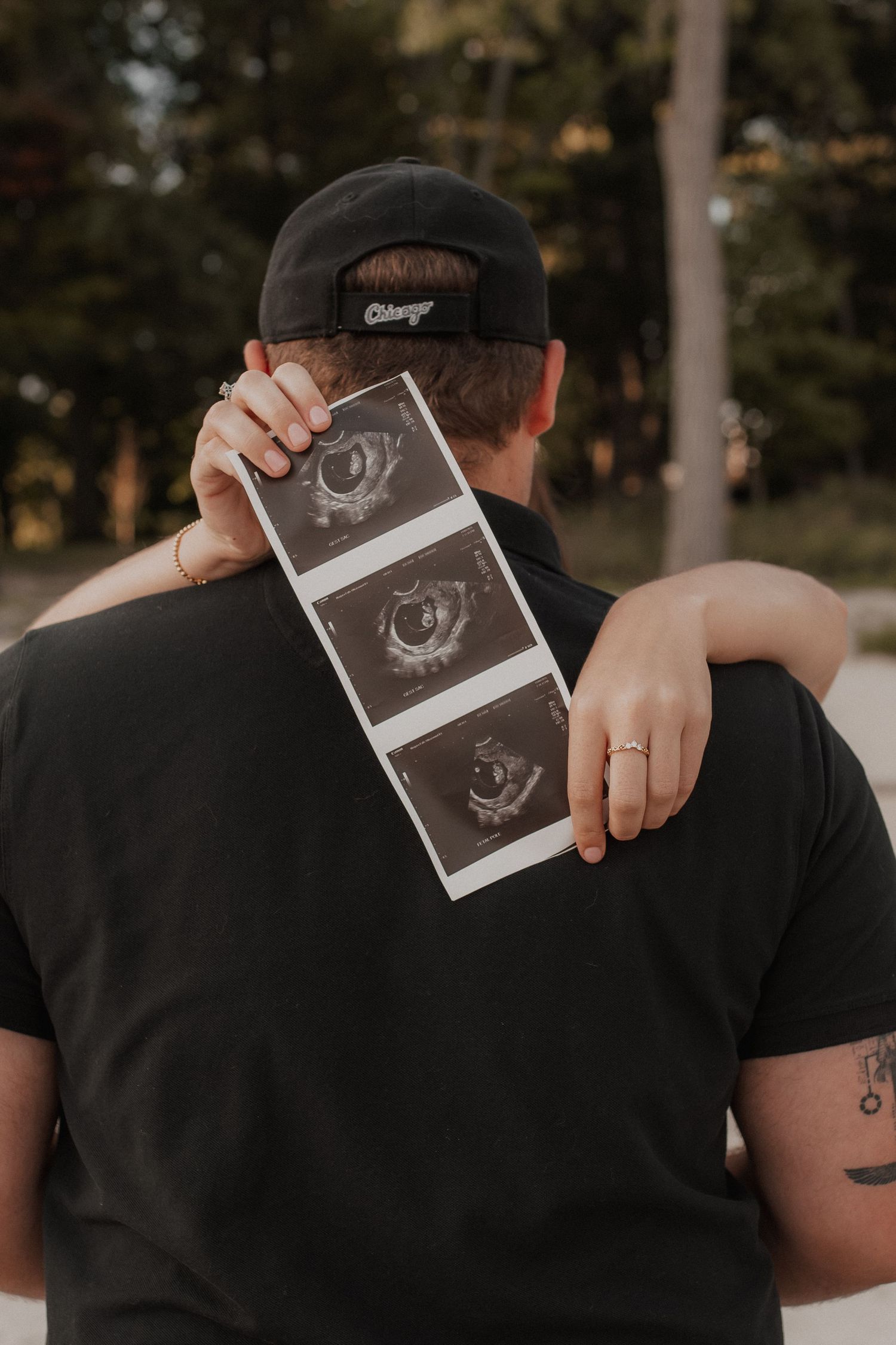 A series of four photos showing hands holding up an ultrasound image while embracing in a tender moment outdoors.