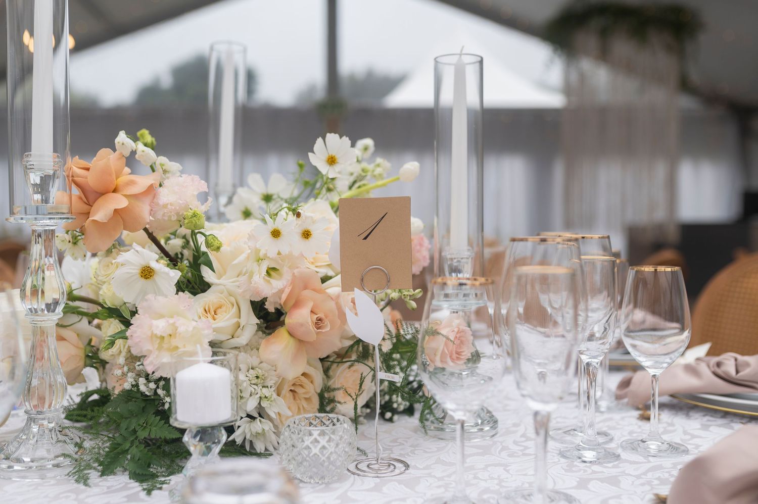Elegant wedding table settings with crystal glasses, peach floral centerpieces and romantic candlelight decorations.