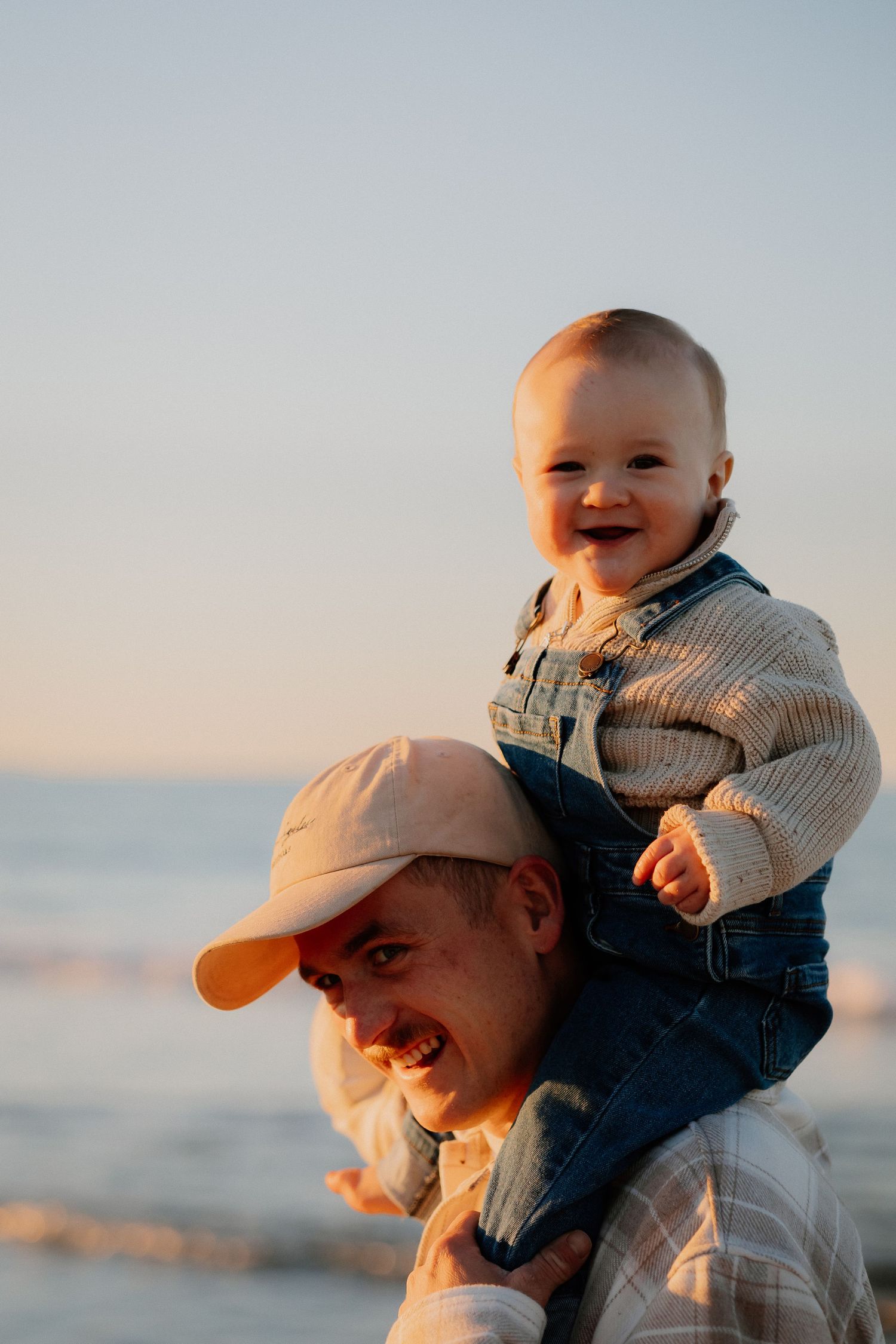 A playful moment between parent and child on the beach at sunset, wearing casual clothing and sharing joyful laughter.