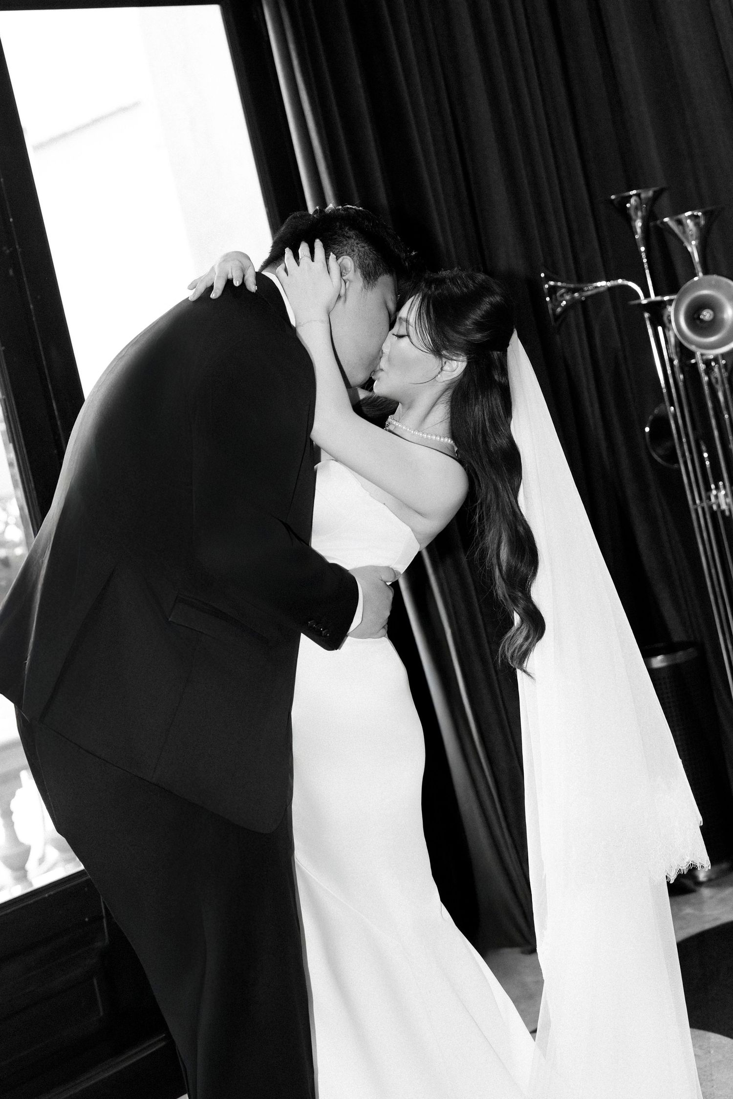 Black and white romantic photo of bride and groom sharing first kiss in elegant wedding venue.