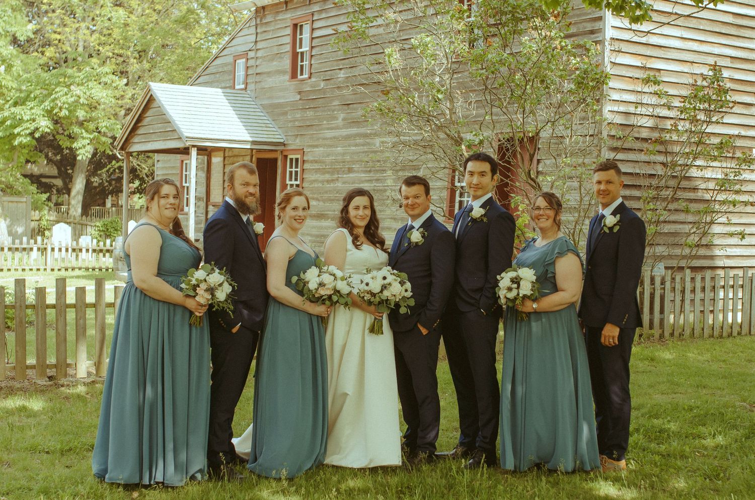 Wedding party lined up outdoors wearing blue bridesmaid dresses and formal attire.