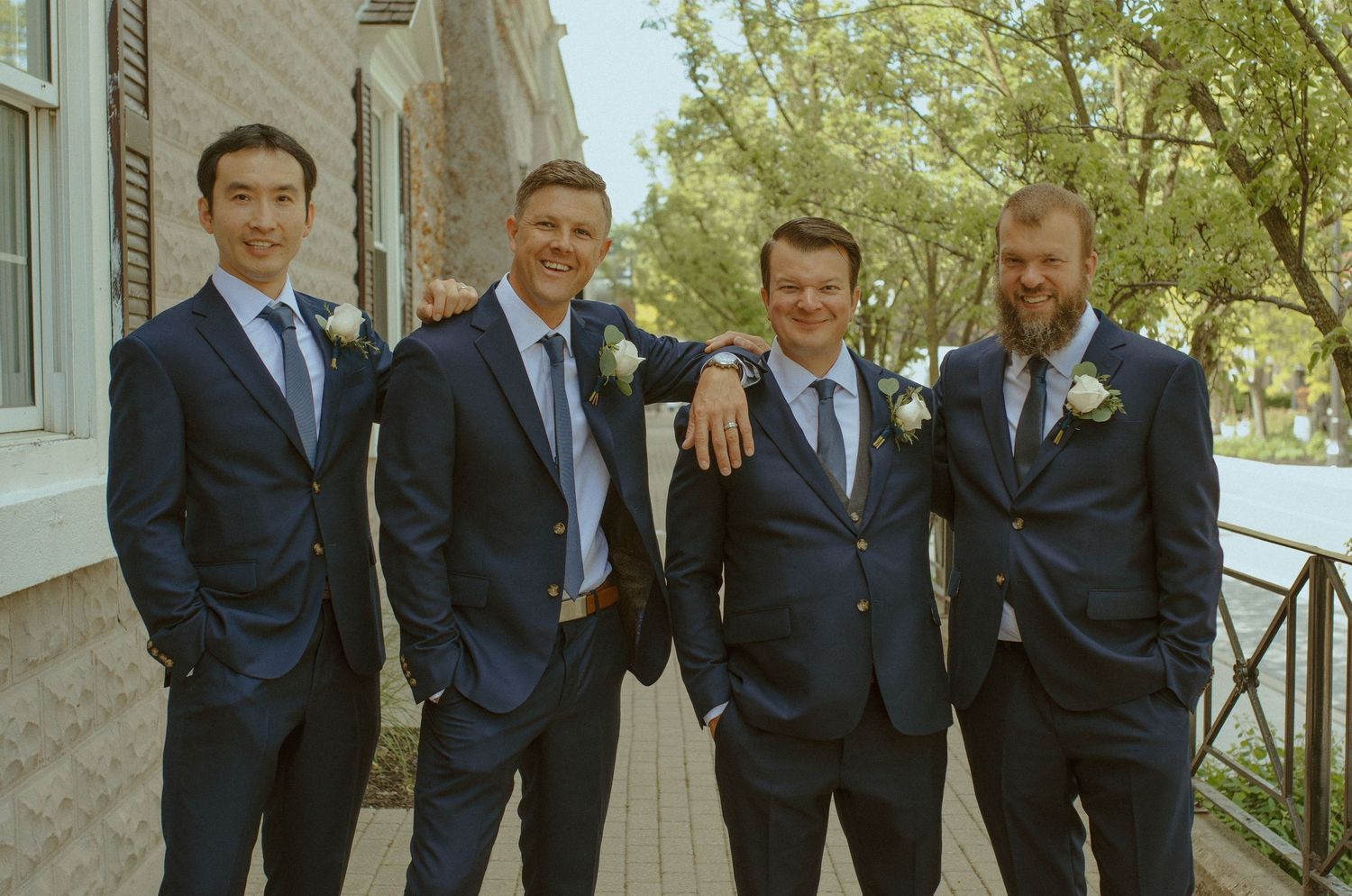 Groomsmen in navy suits pose casually together outside on a wedding day.