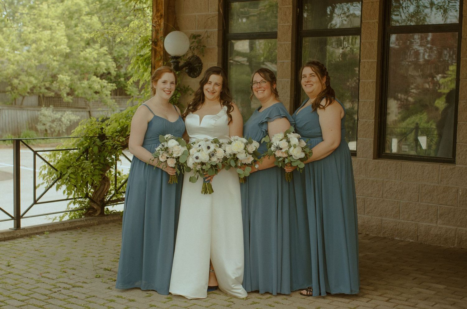 Bridesmaids in dusty blue dresses pose with bride in elegant white gown.