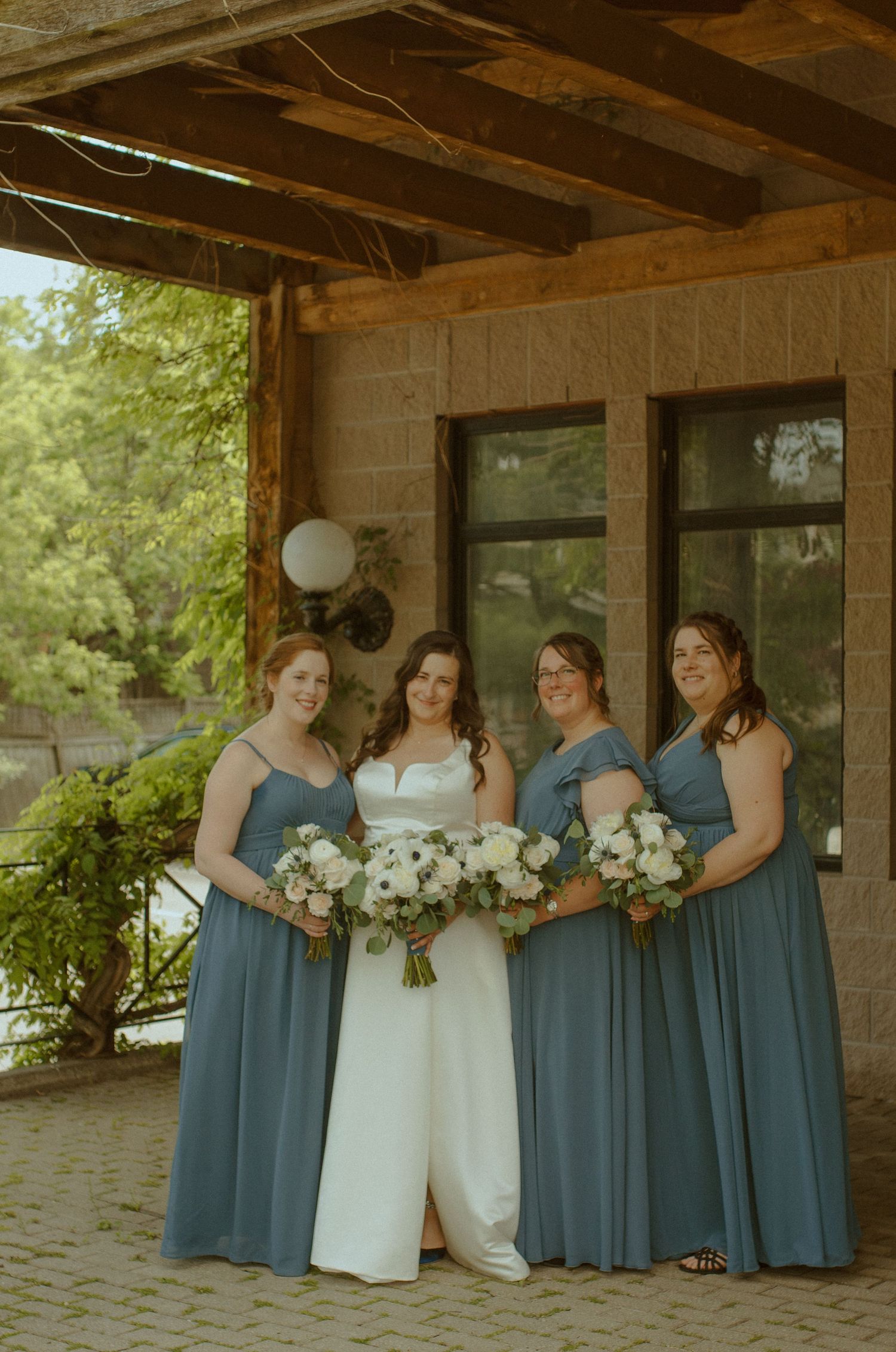Bridesmaids in blue dresses standing with bride in white against rustic stone backdrop.