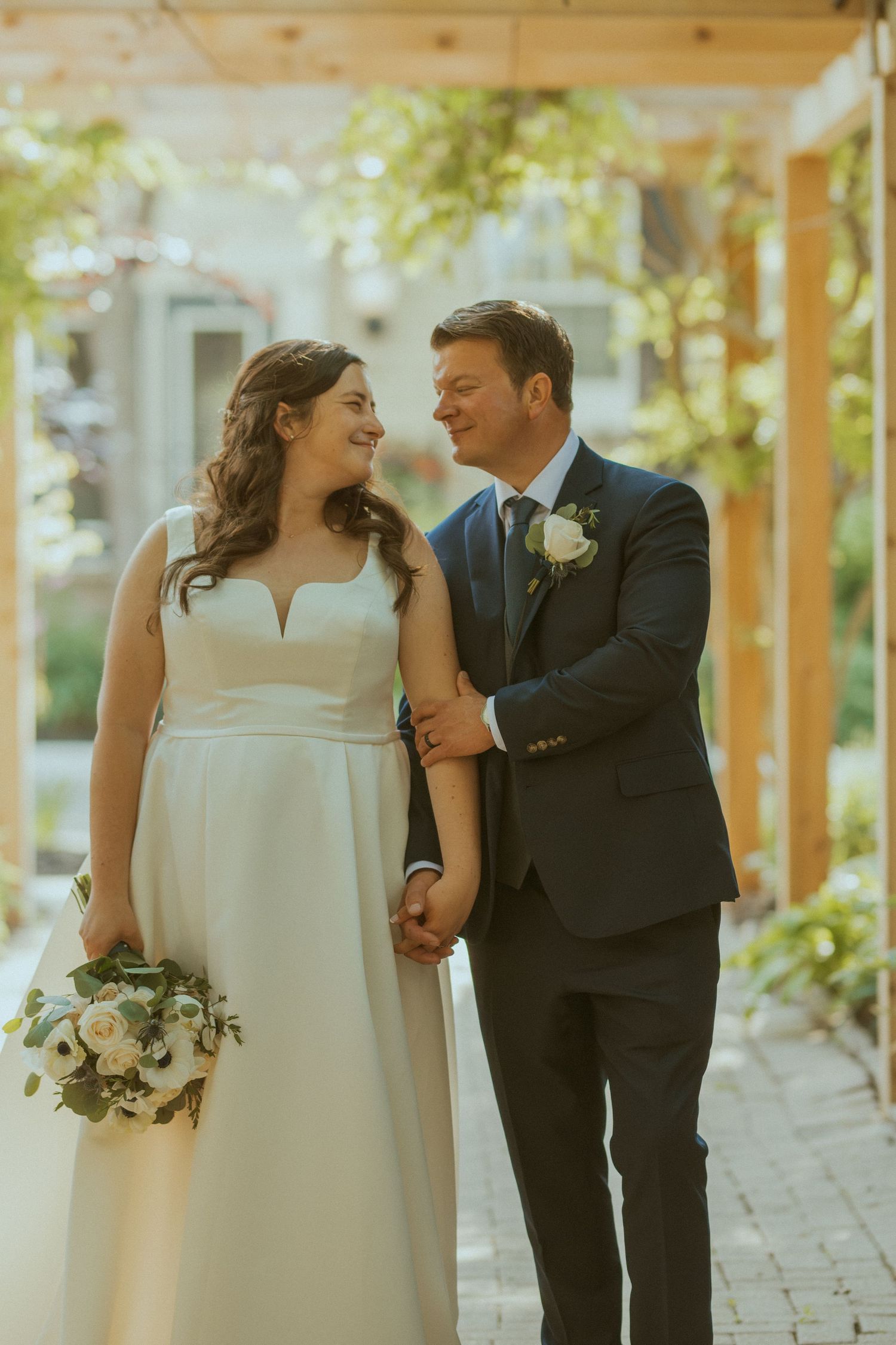 A romantic wedding moment captured between newlyweds on a brick pathway surrounded by greenery.