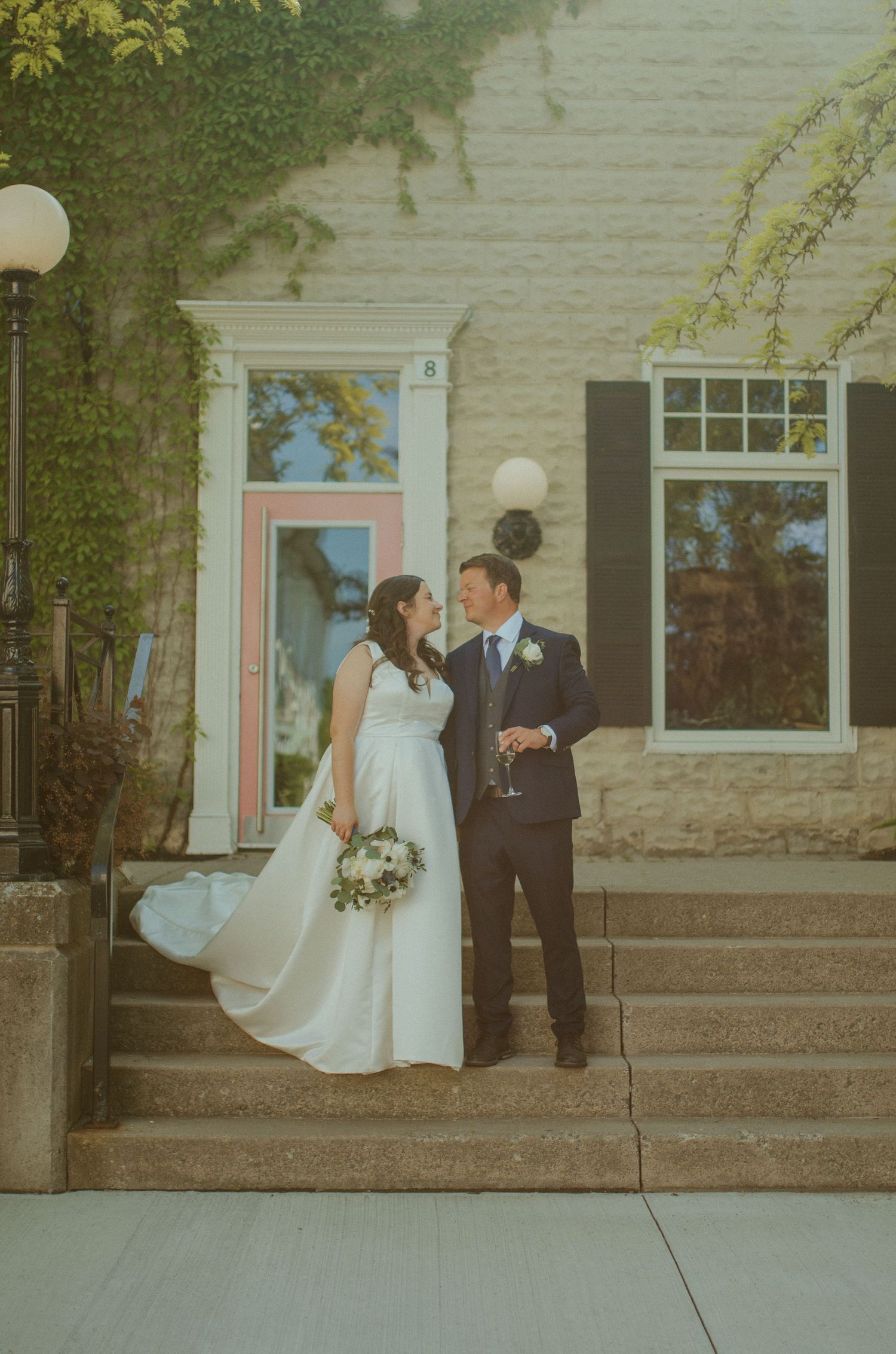 A wedding couple shares an intimate moment on stone steps outside a historic building.