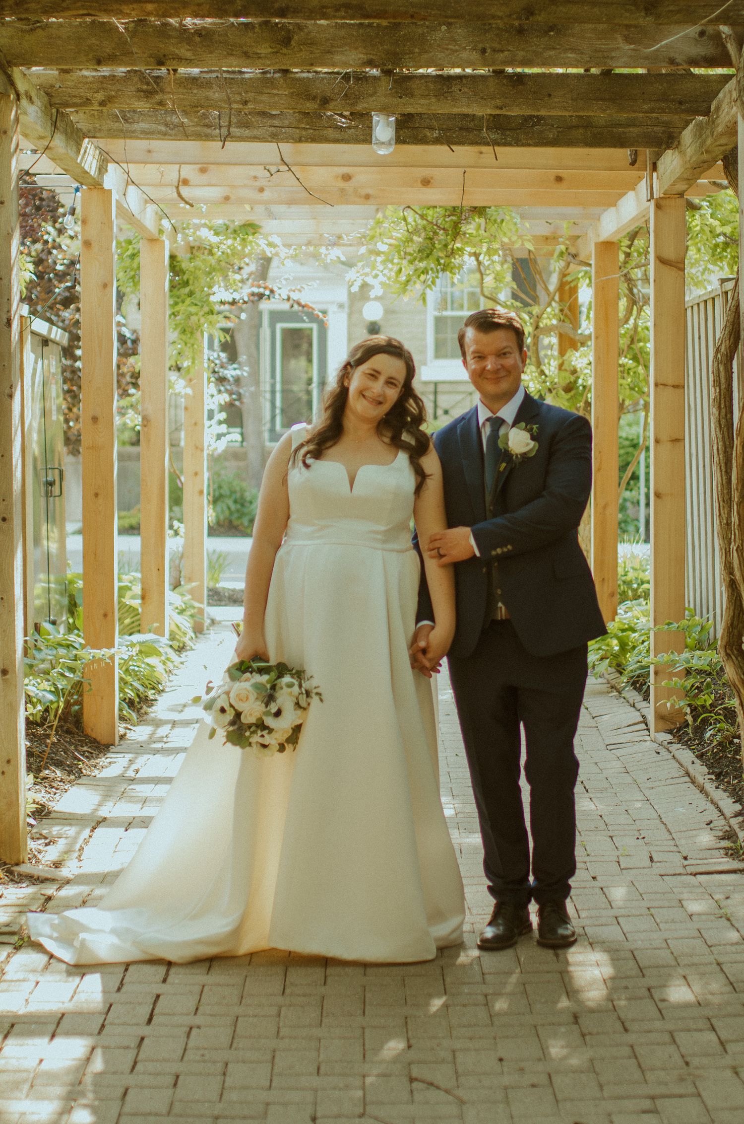 A couple poses under a flower-adorned pergola during their wedding ceremony.