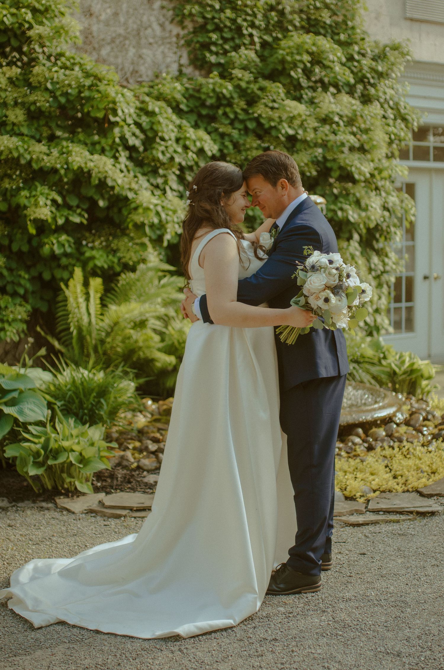 A tender wedding moment captured in a garden setting with lush green foliage.